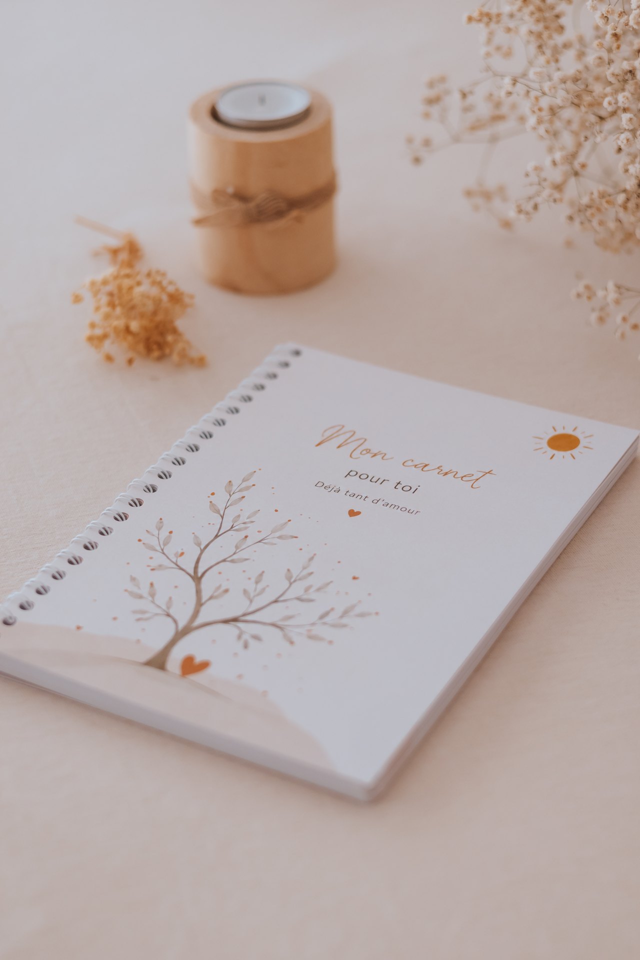 Carnet de grossesse à reliure spirale posé près d'une bougie et de fleurs séchées — Entre Deux