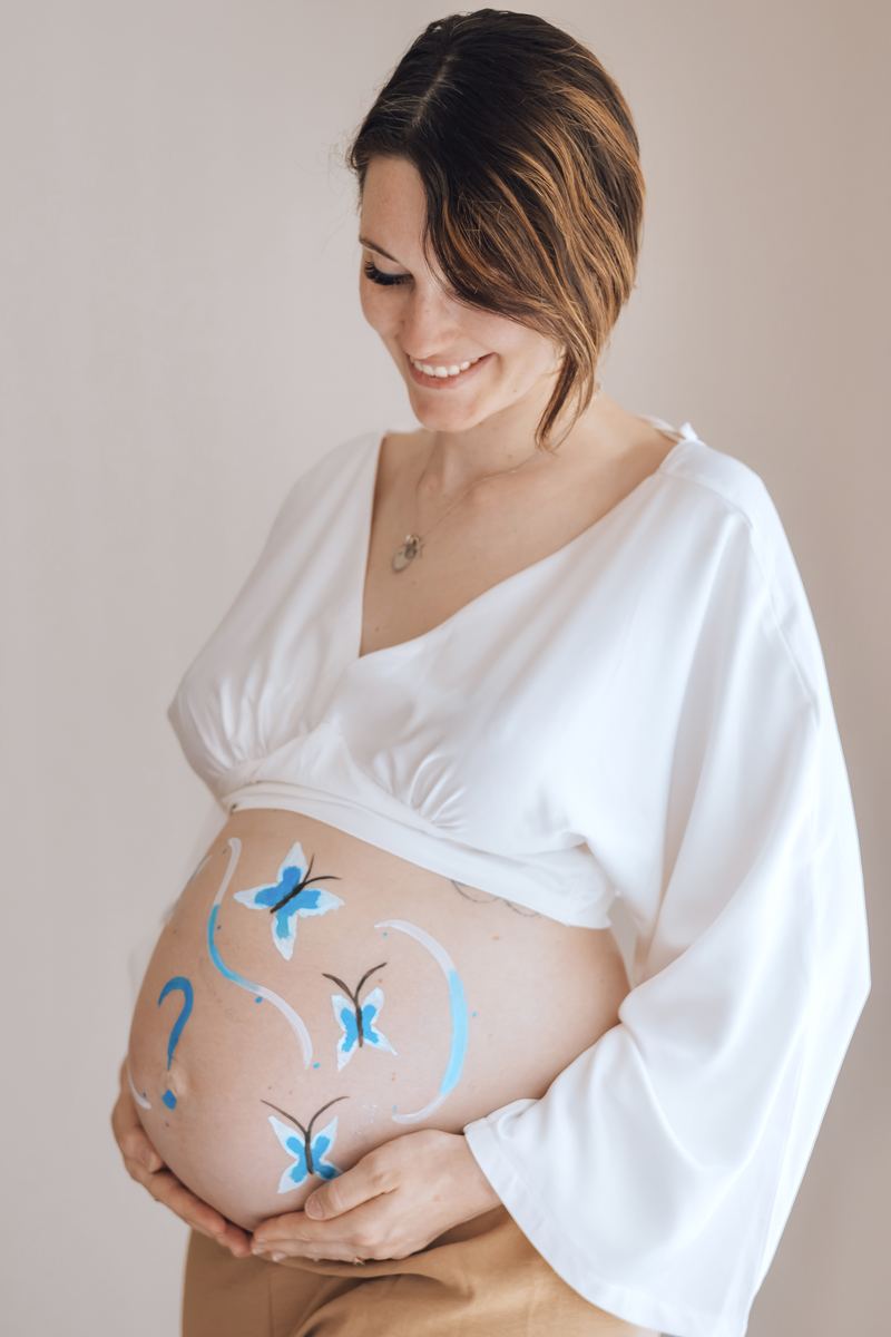 Ventre de future maman peint de papillons bleus, les mains posées de chaque côté — Entre Deux
