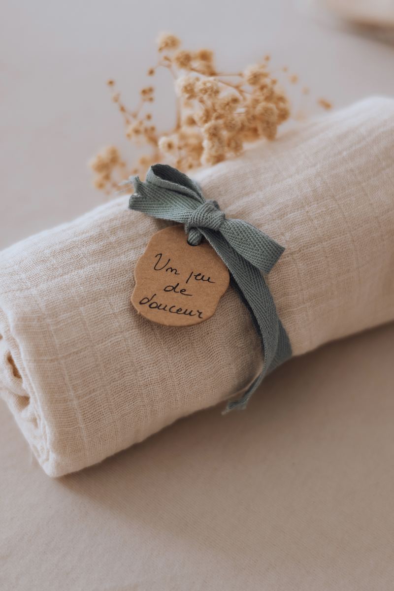 Lange en gaze de coton roulé, noué d'un ruban vert et d'un médaillon en bois gravé — Entre Deux