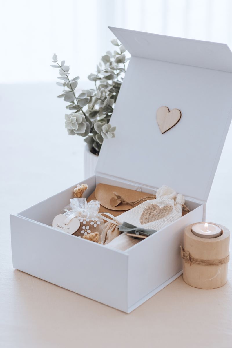 Le coffret des premiers liens garni : pochettes, cœur en bois et fleurs séchées, près d'une bougie — Entre Deux