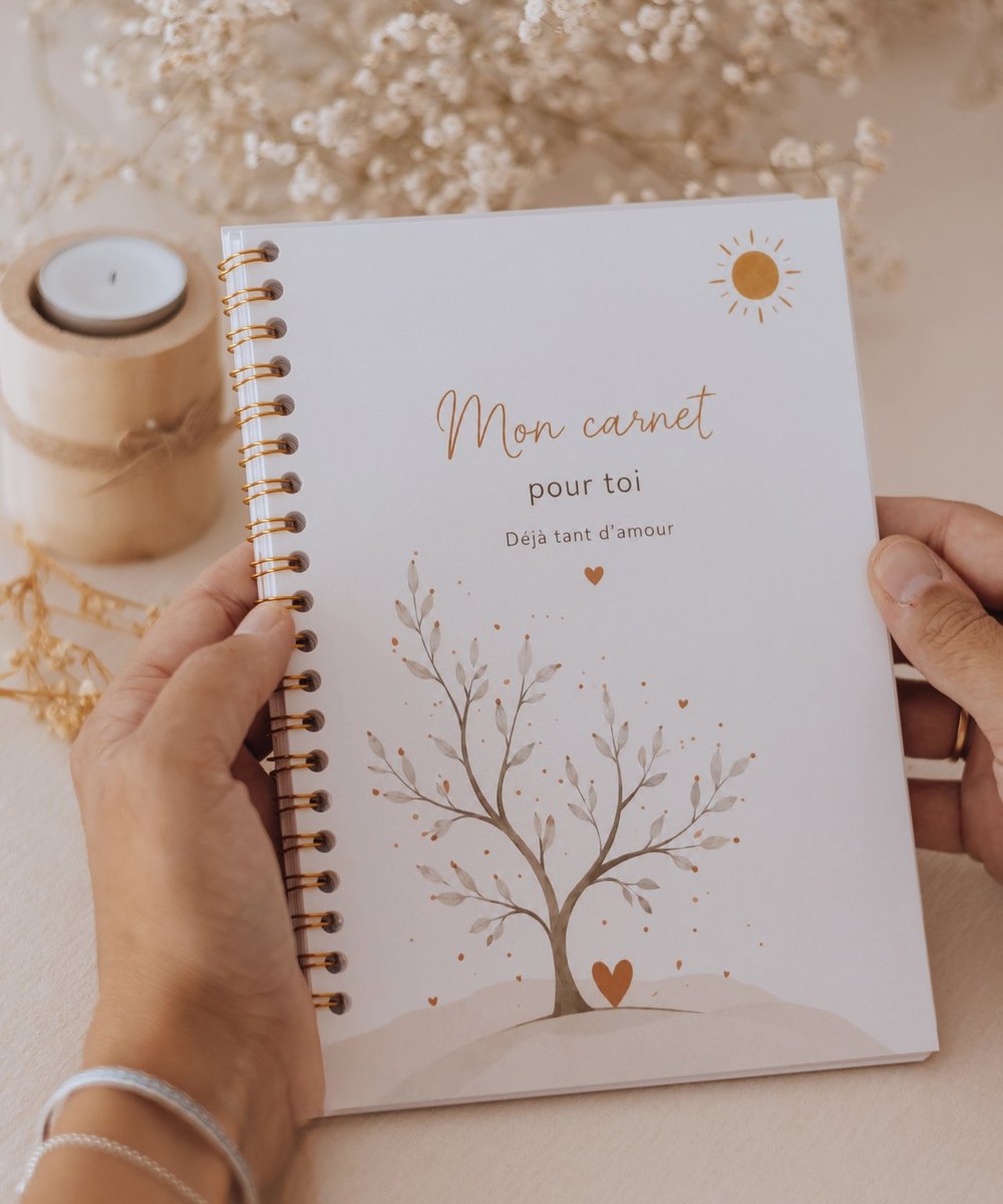 Carnet de grossesse « Mon carnet pour toi » tenu à deux mains, bougie et fleurs séchées — Entre Deux