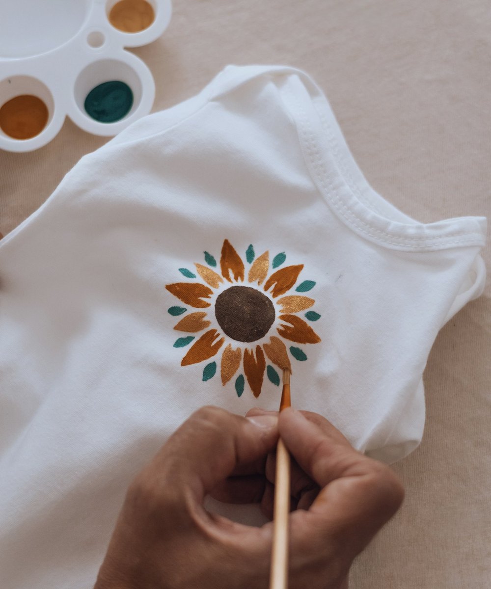 Body de naissance peint à la main d'un tournesol, pinceau et palette de couleurs — Entre Deux