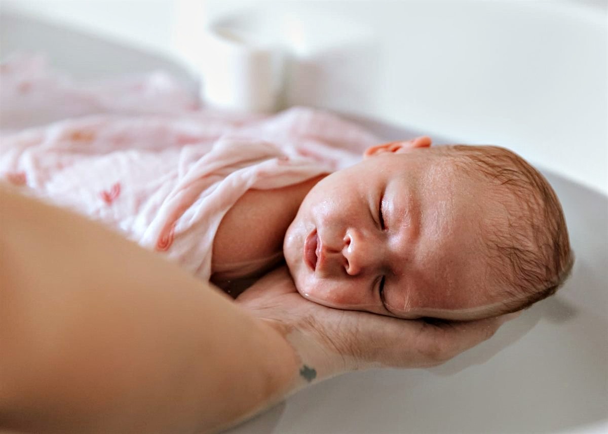 Bébé au creux de la main pendant le bain enveloppant — Entre Deux